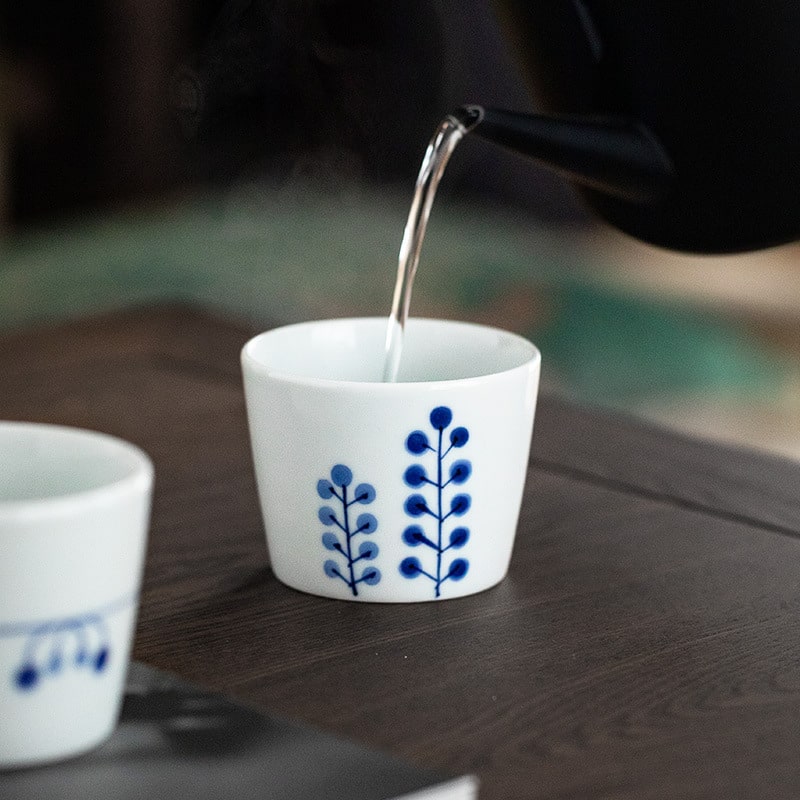 Japanese tea cup being filled with water, showcasing underglaze floral pattern.