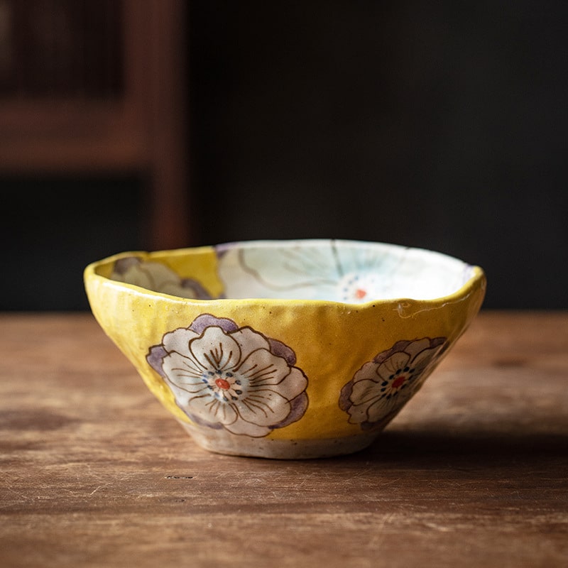 Handcrafted Japanese ceramic bowl with yellow floral designs on a wooden surface