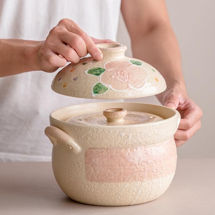 Hand lifting the lid of a Japanese Wan Gu-yaki rice and soup pot