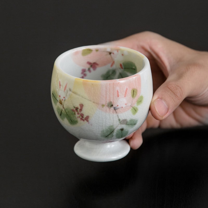 Hand holding a whimsical ceramic cup with watercolor details