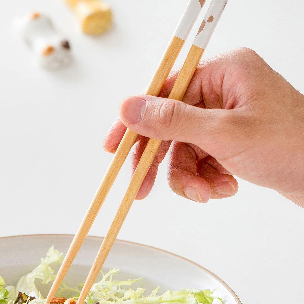 Hand using white cat paw chopsticks to enjoy a salad