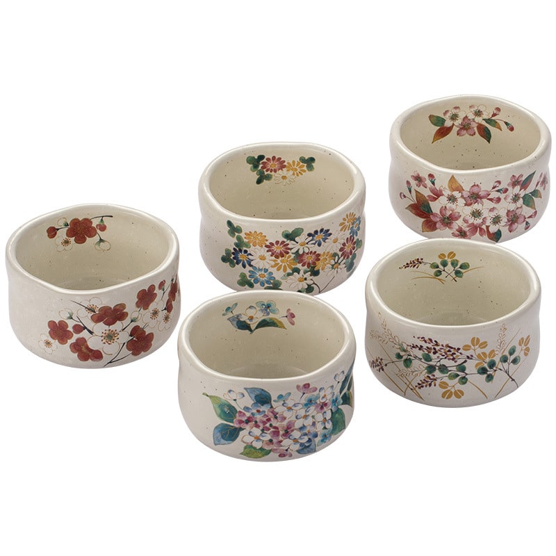 Set of white ceramic cups with colorful floral artwork displayed on wooden shelves