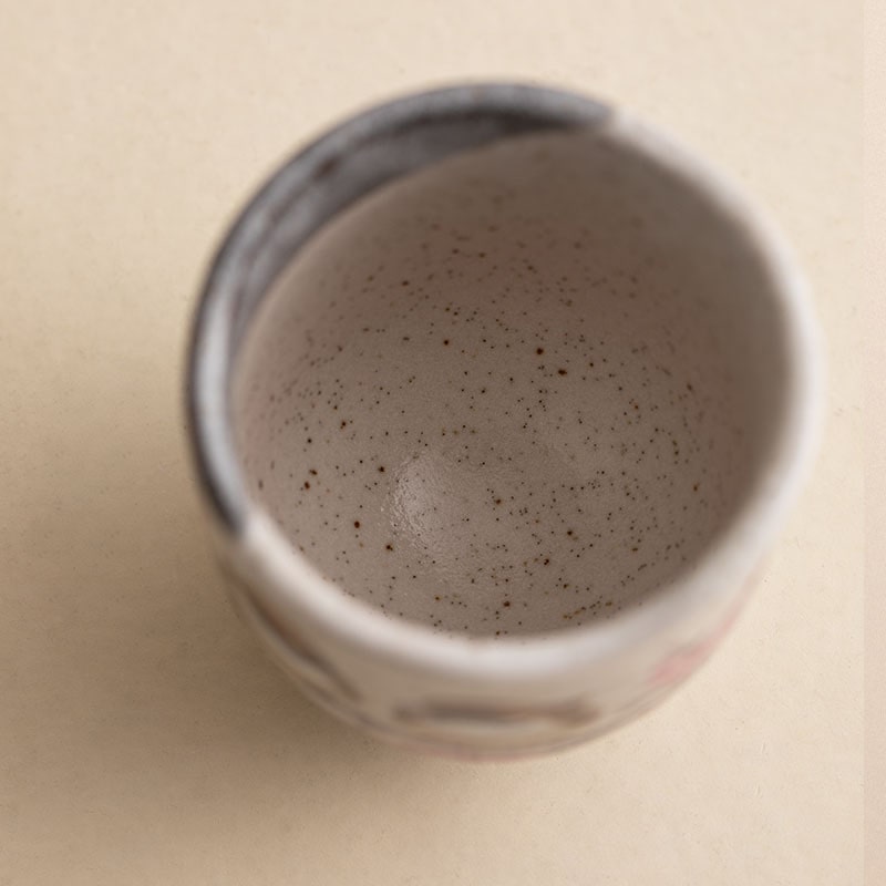 Speckled ceramic cup with cherry blossom artwork.