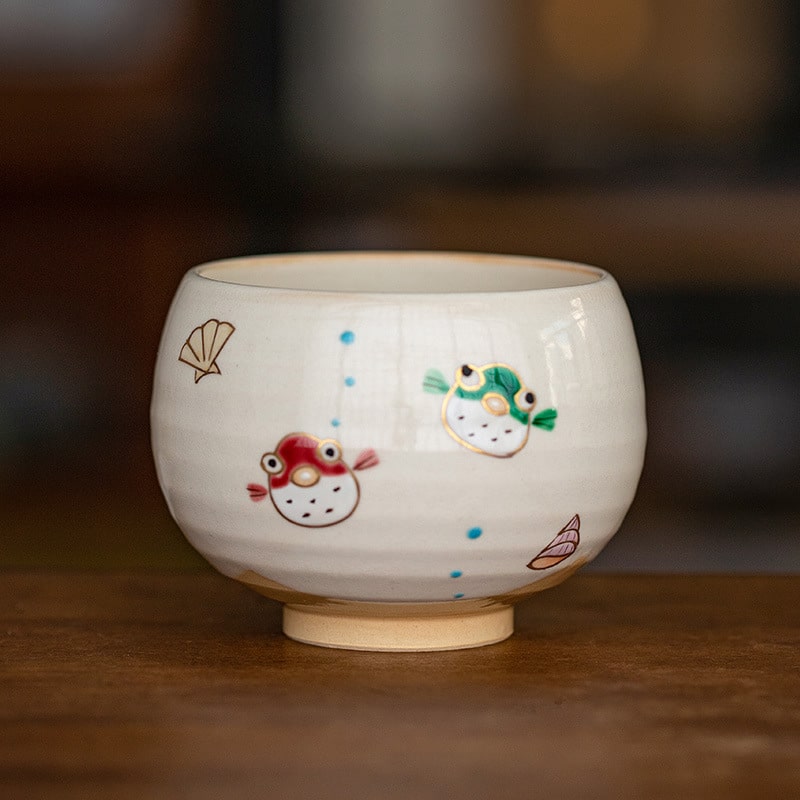 Hand holding a hand-painted ceramic cup with cheerful designs.