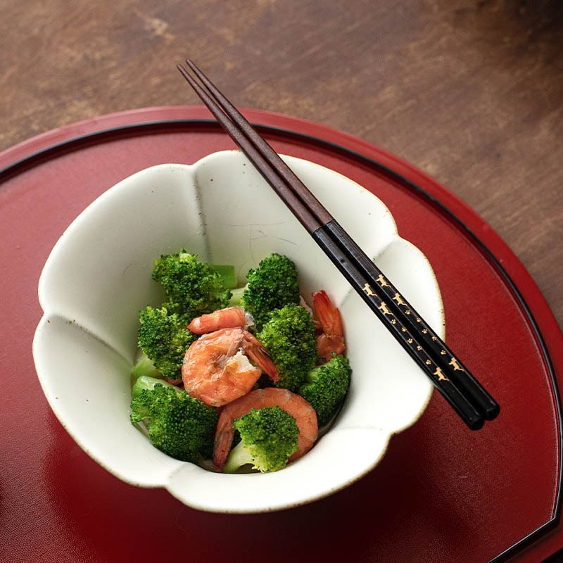 Black lacquer chopsticks resting on a bowl of broccoli and shrimp