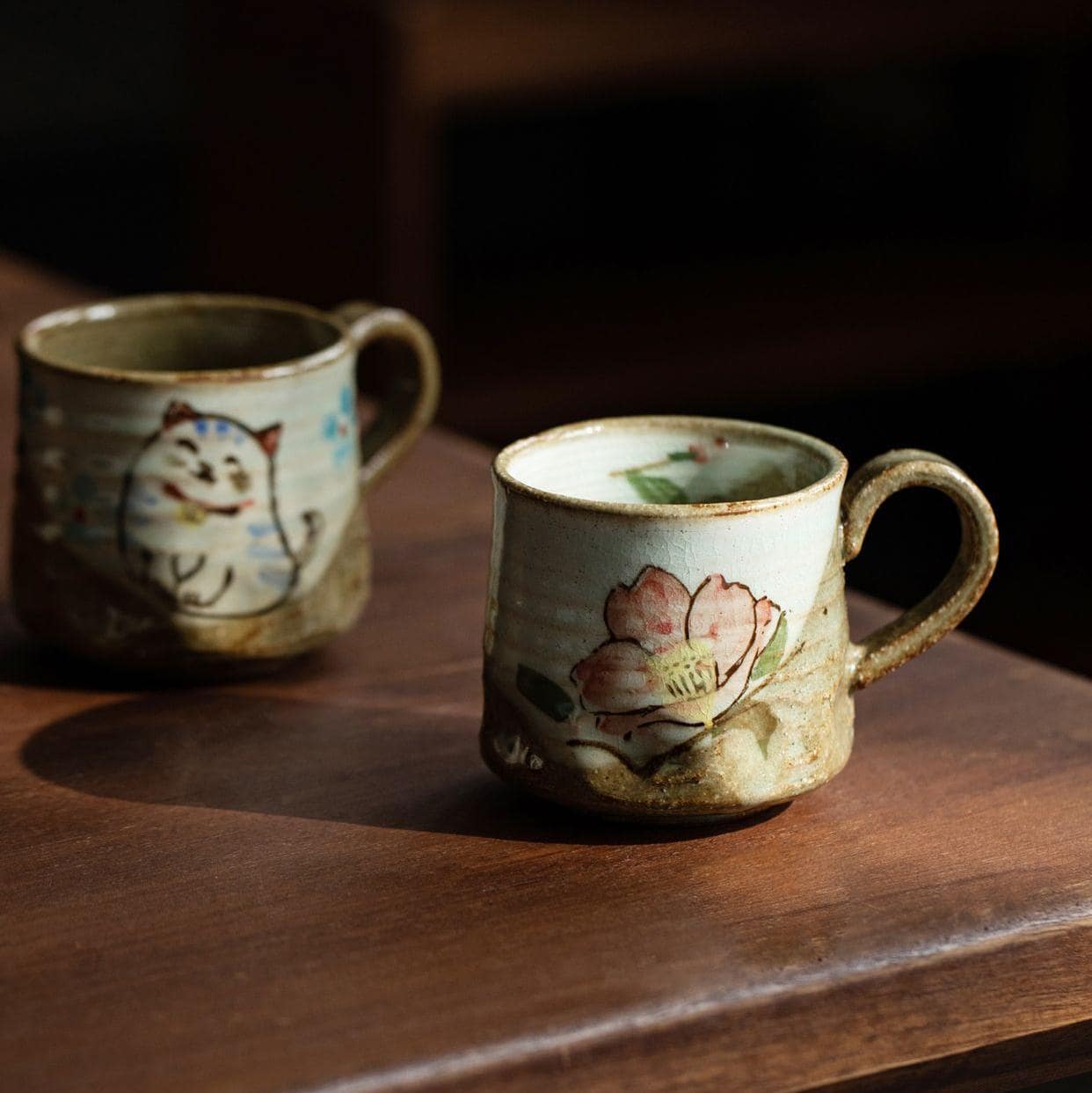 Pair of rustic animal-themed ceramic cups on a wooden table.