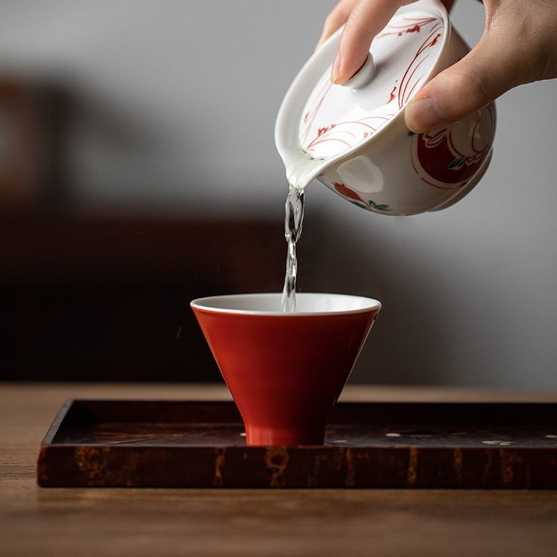 Porcelain teacup pouring tea into a matching red cup