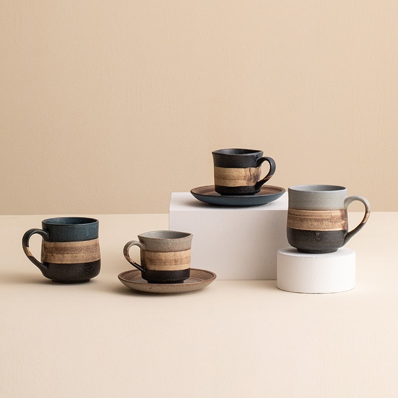 Handcrafted ceramic coffee cup with two-tone design and saucer.