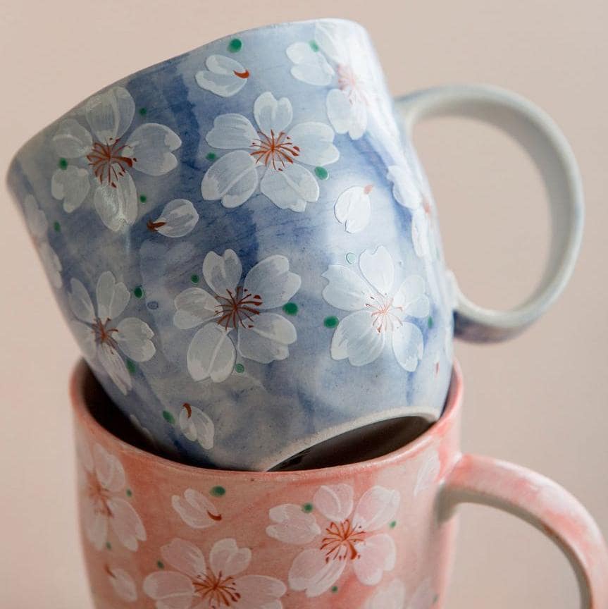 Blue hand-painted cherry blossom coffee cup on a wooden table.