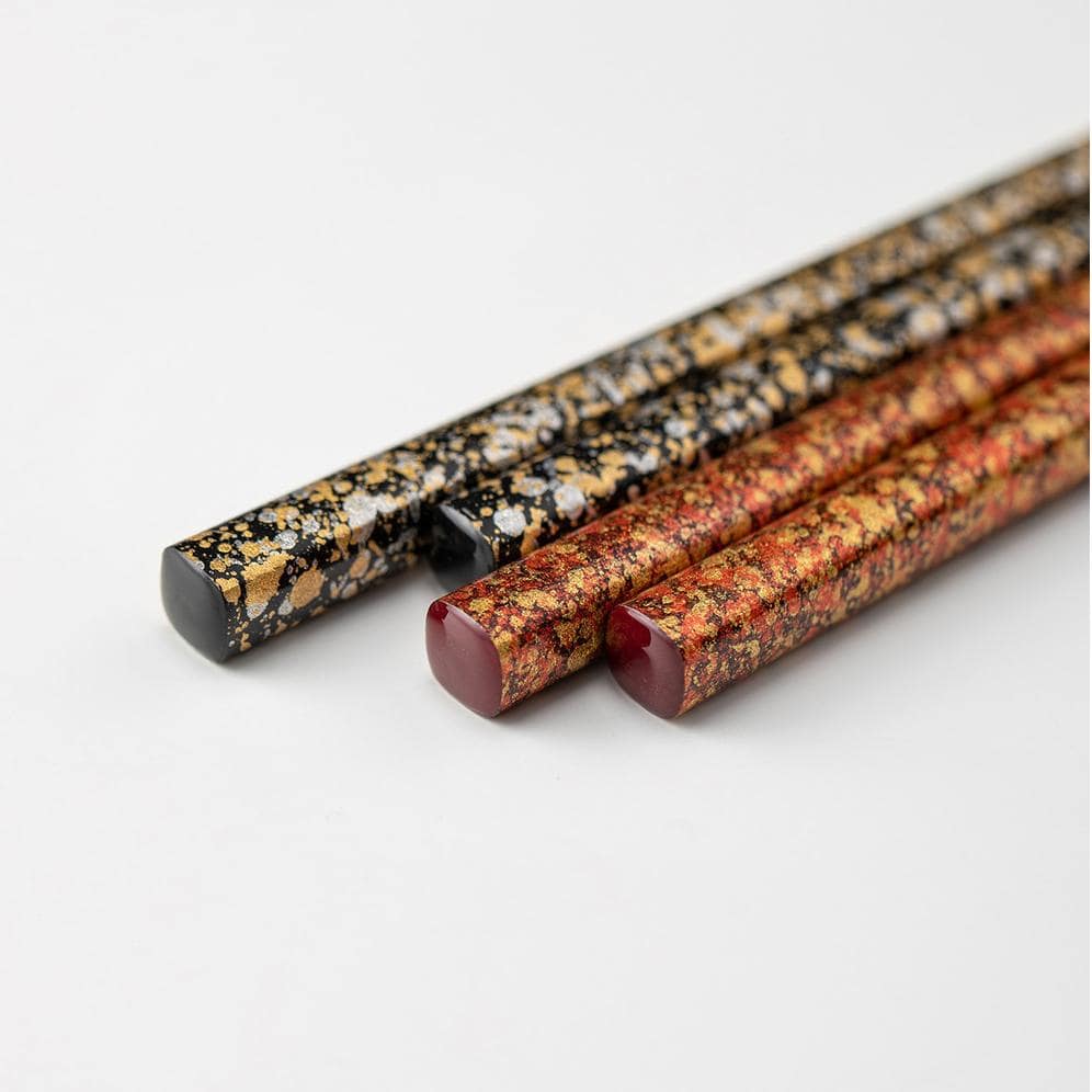 Close-up of gold and speckled lacquered chopsticks on white plate