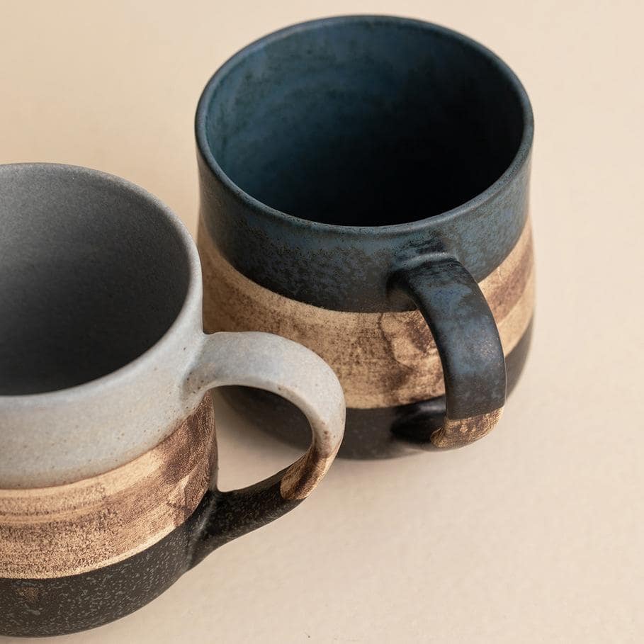 Handcrafted ceramic coffee cup with two-tone design and saucer.