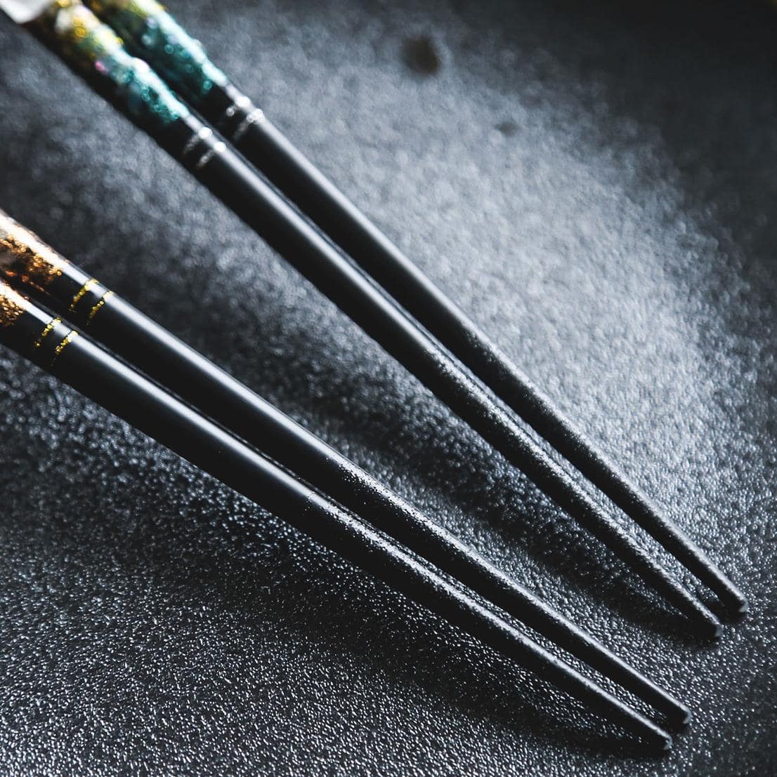 Elegant reusable chopsticks placed on a black dish.