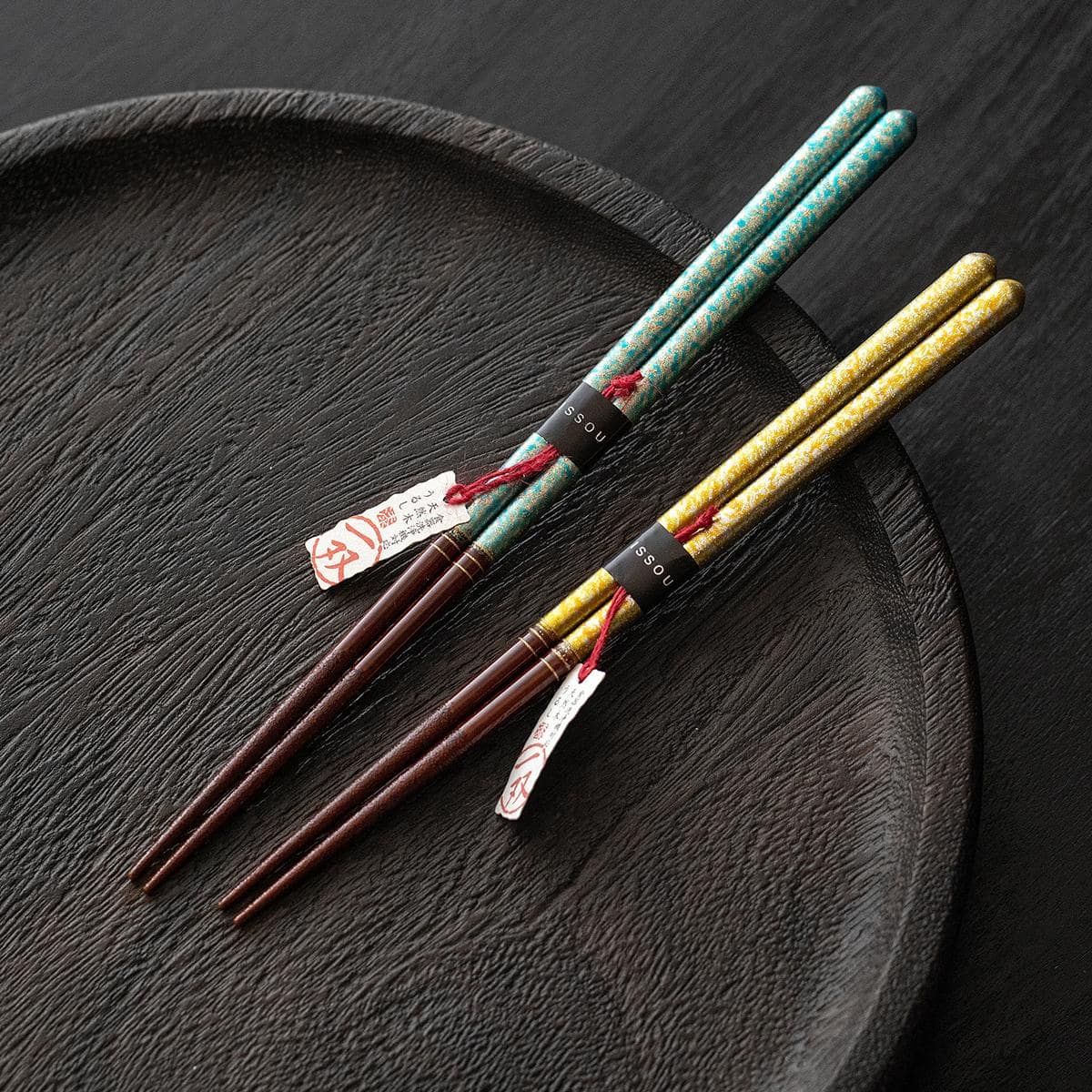 Close-up of ISHIDA Japanese wooden chopsticks with gold and turquoise patterns.