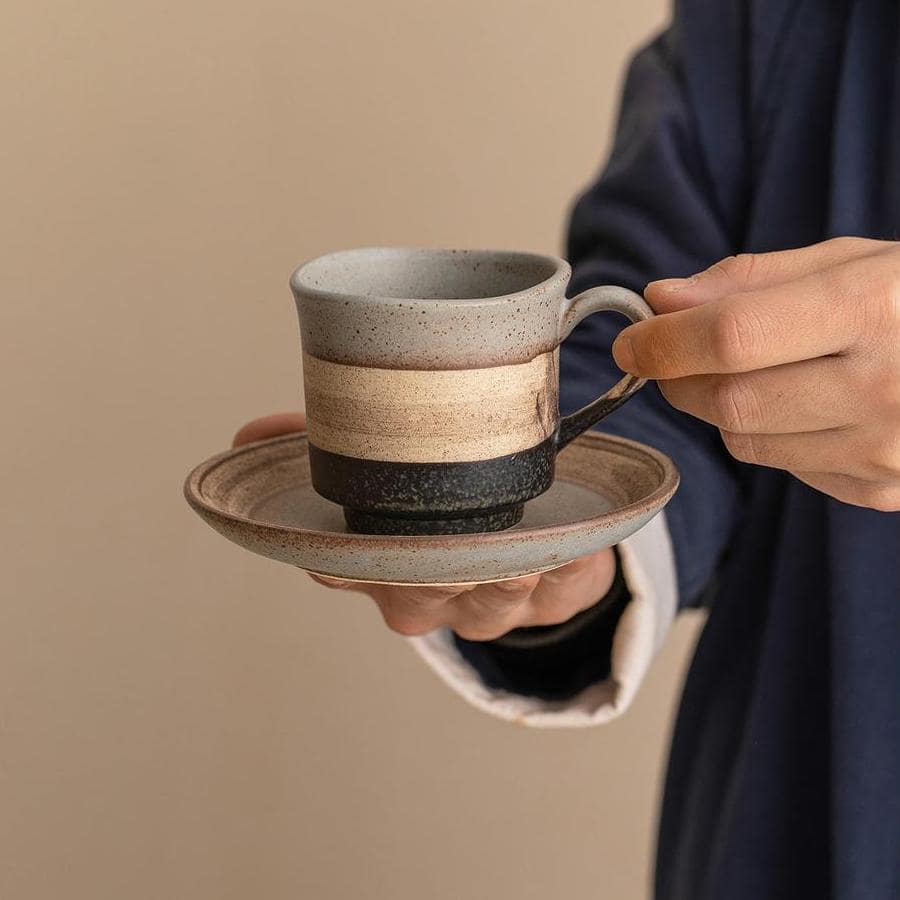 Rustic ceramic coffee mug with earthy tones on a saucer.