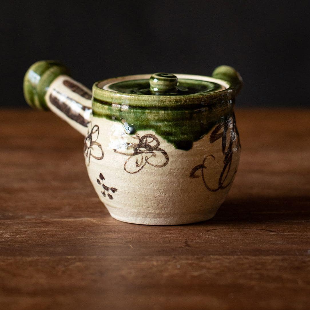 Artisan-crafted Oribe teapot pouring tea into a matching cup.