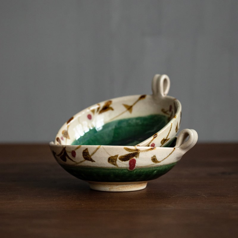 Stack of green floral ceramic bowls with decorative handle