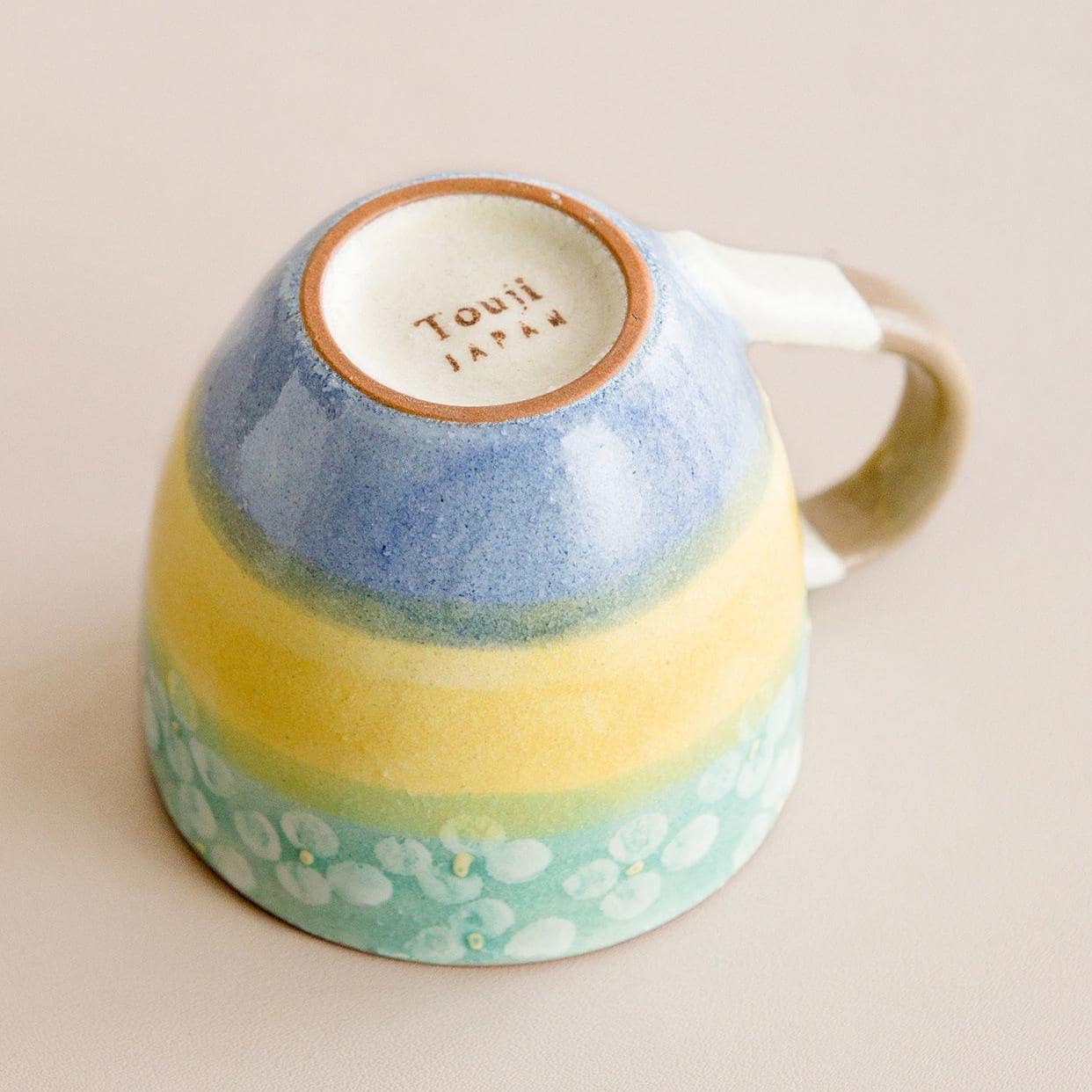 Close-up of a yellow, blue, and green ceramic cup bottom with branding