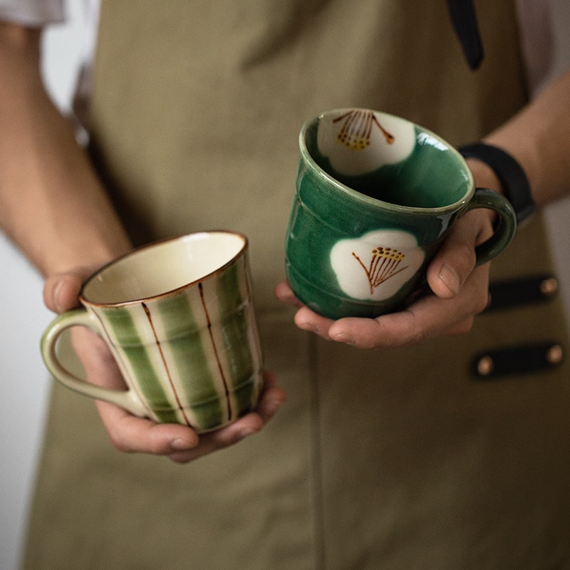 Green and striped ceramic mugs held in hands