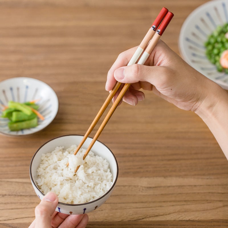 Hand using panda-themed chopsticks to pick up rice