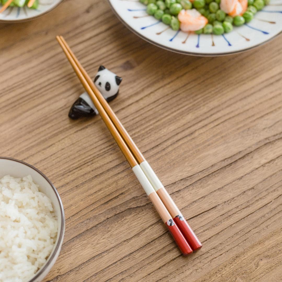 Hand using panda-themed chopsticks to pick up rice