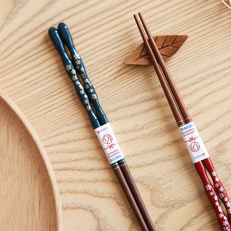 Hand holding red sakura lacquered chopsticks over sushi