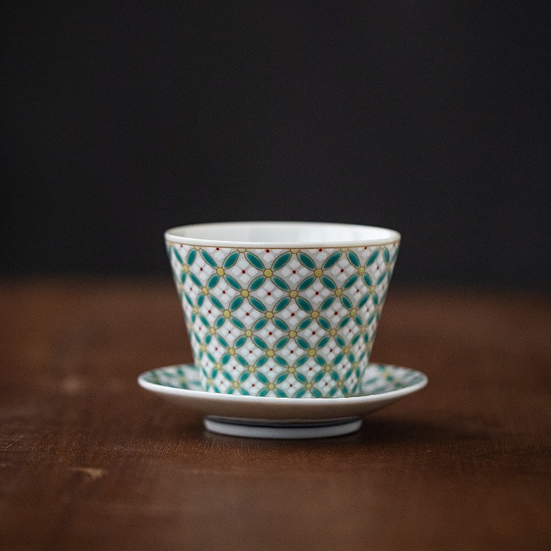 Hand holding a vibrant geometric ceramic cup with teal and yellow patterns.