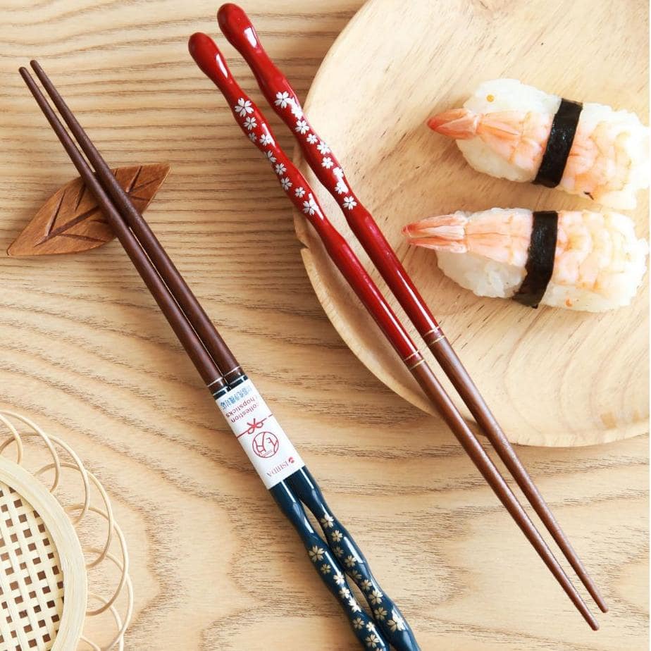 Hand holding red sakura lacquered chopsticks over sushi