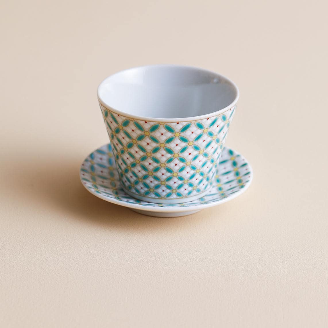 Hand holding a vibrant geometric ceramic cup with teal and yellow patterns.