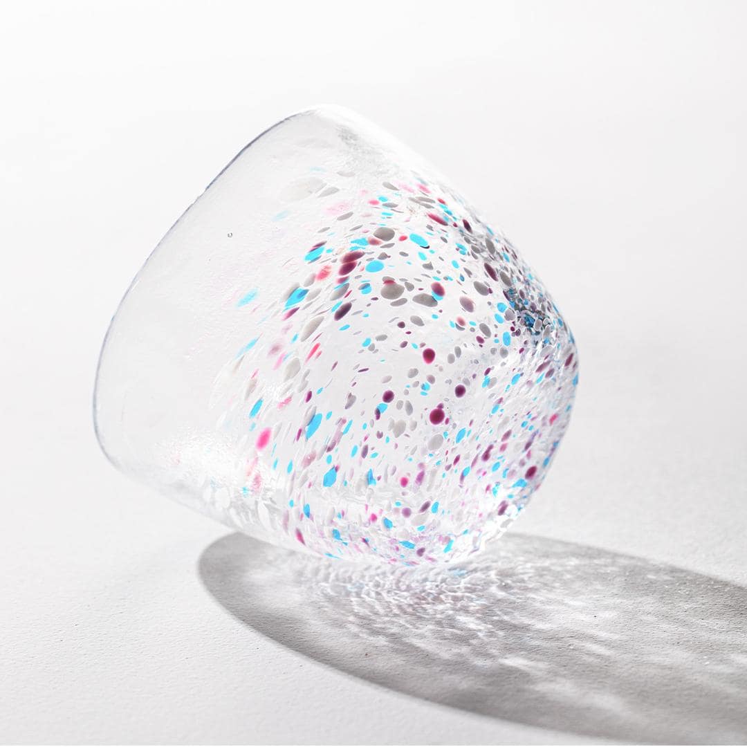 Hand-blown colorful artisan glass cup on white background.