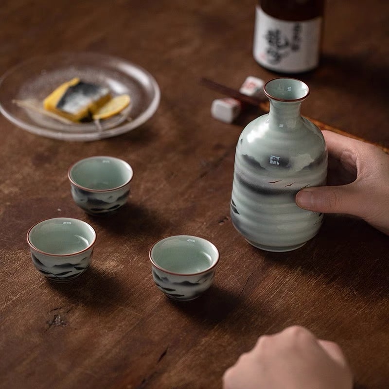 Elegant soft green sake bottles and matching cups on a wooden table.
