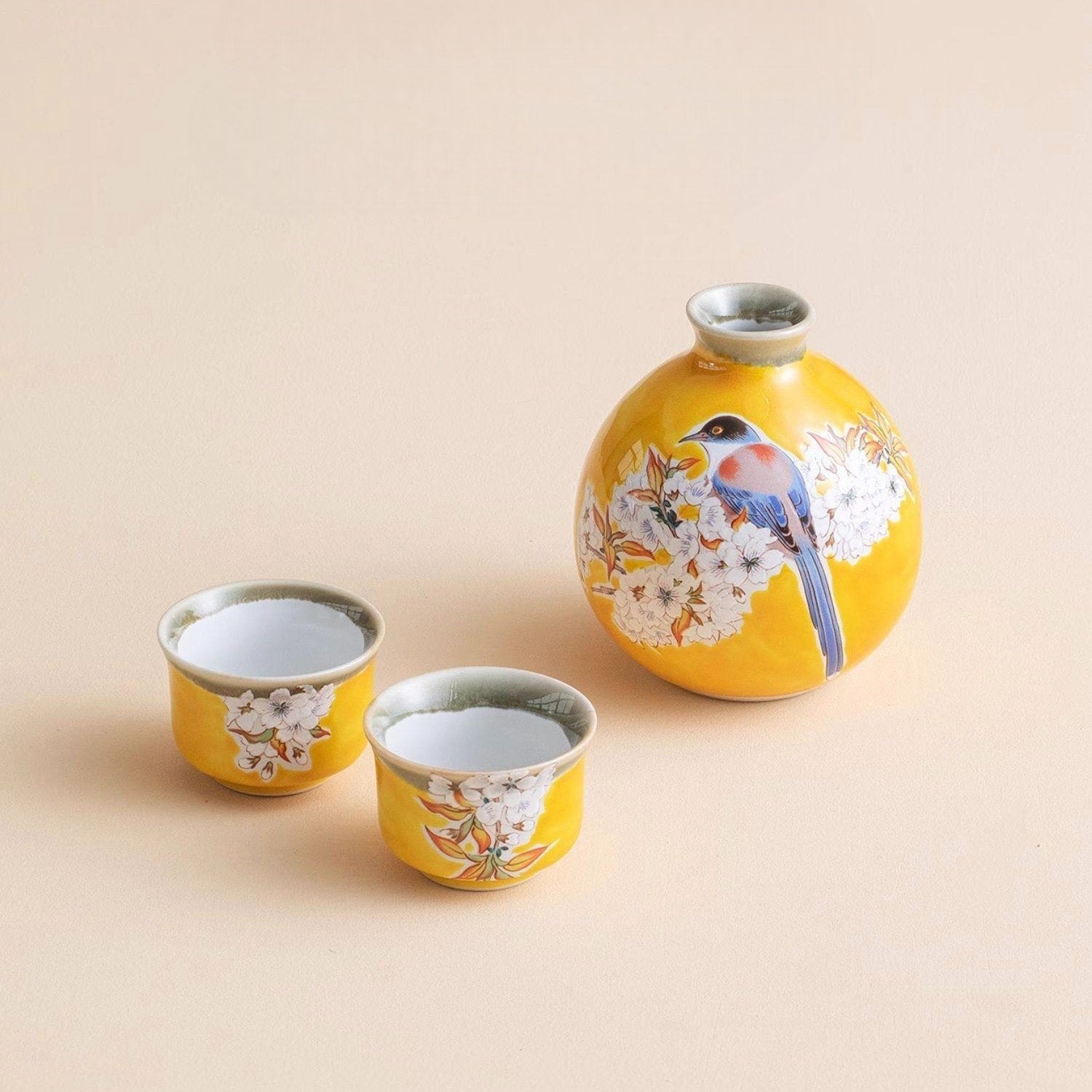 Vibrant yellow ceramic sake set with bird and cherry blossom designs.
