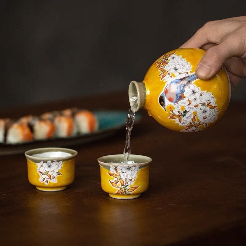 Vibrant yellow ceramic sake set with bird and cherry blossom designs.
