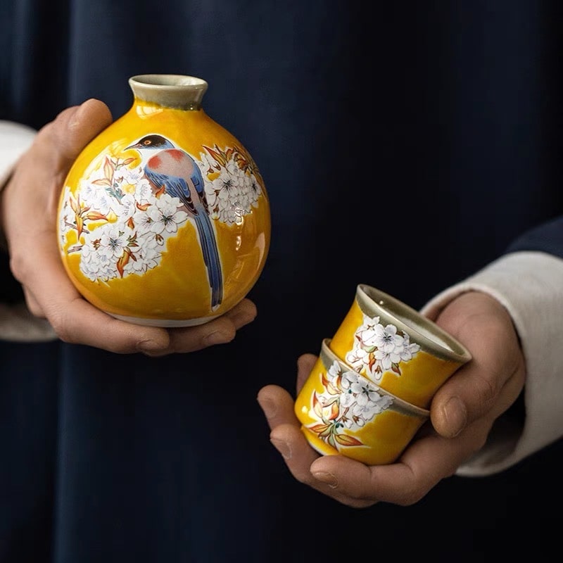 Close-up of ceramic sake cups with cherry blossom and bird details.
