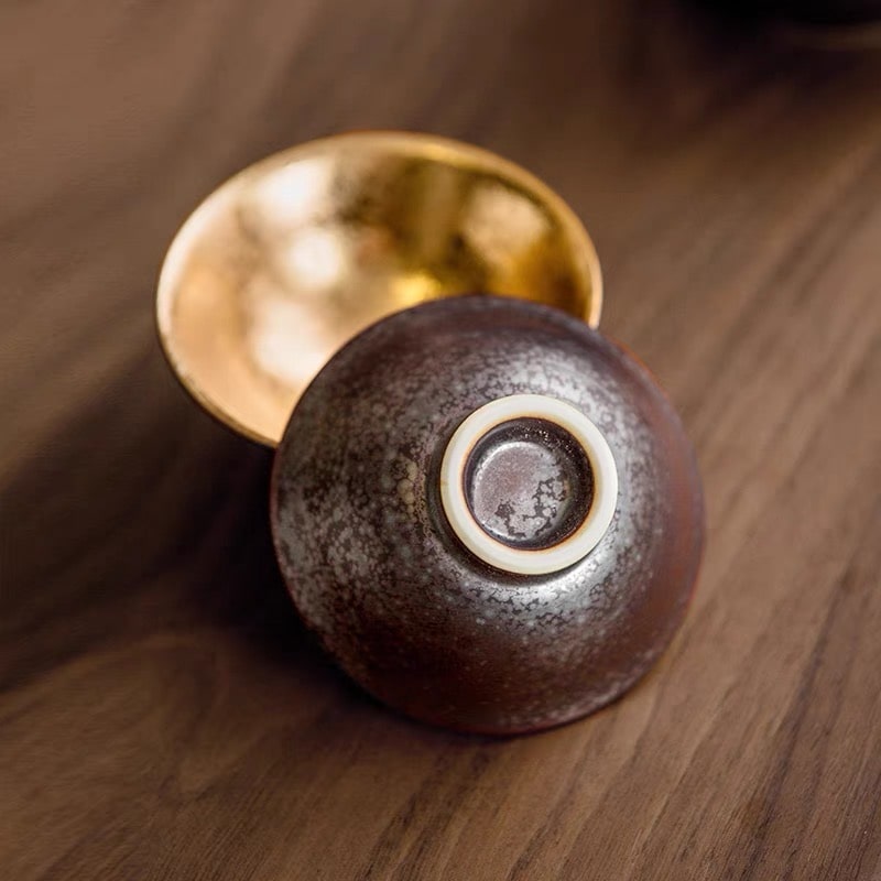 Close-up of golden interior cups paired with a sleek sake bottle.
