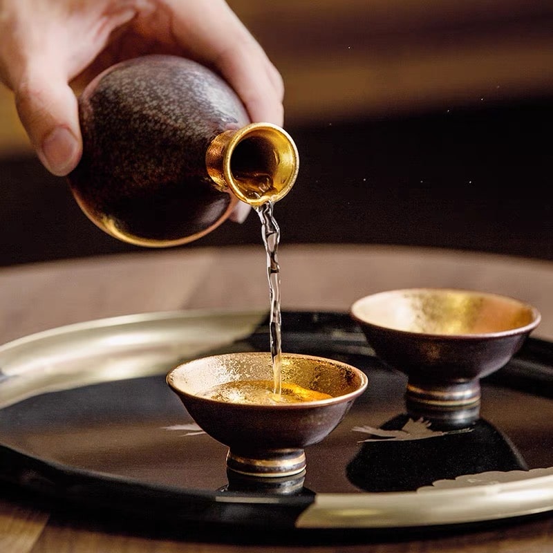 Luxurious sake set with a golden-lined cup and speckled black bottle.
