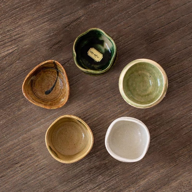 Rustic Japanese sake cups in neutral and green hues on a wooden table.
