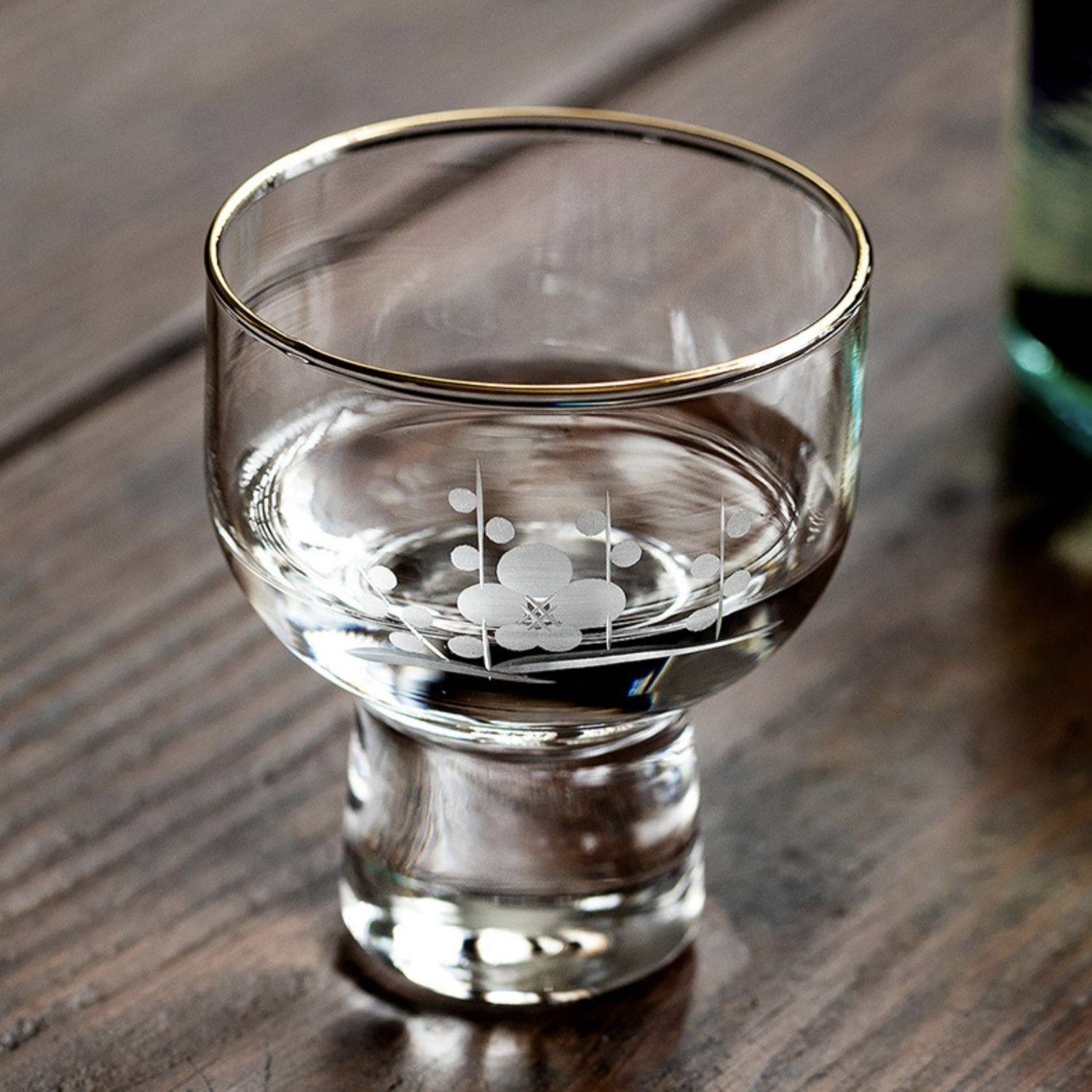 Transparent sake cups with golden rims and traditional Japanese motifs.
