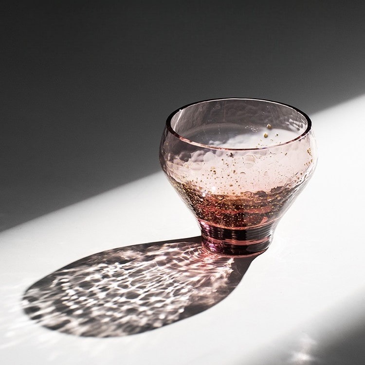 Pink glass sake cup with gold accents and rounded design.
