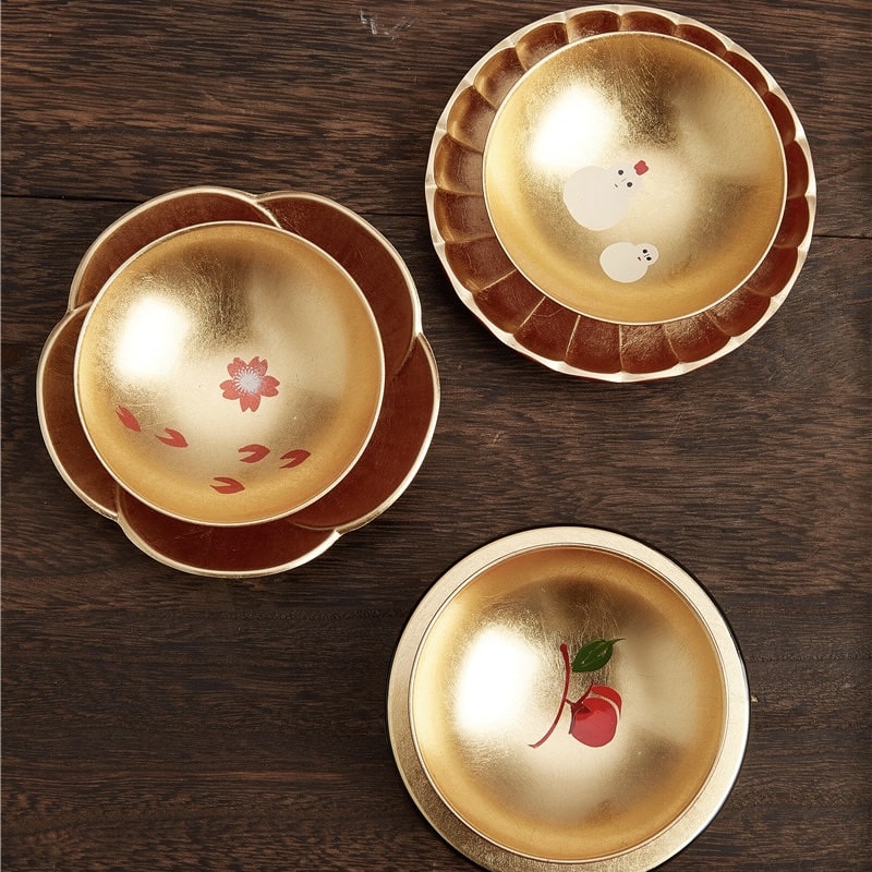 Close-up of traditional lacquer sake cups featuring seasonal icons.
