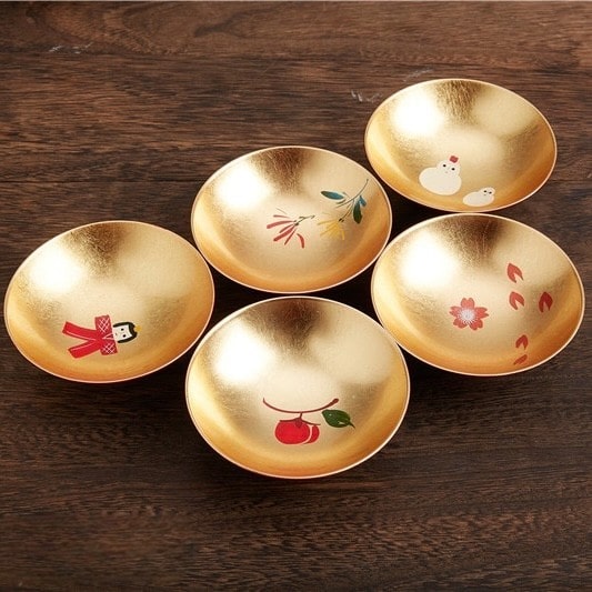 Artistic gold and red sake cup set displayed on a wooden table.
