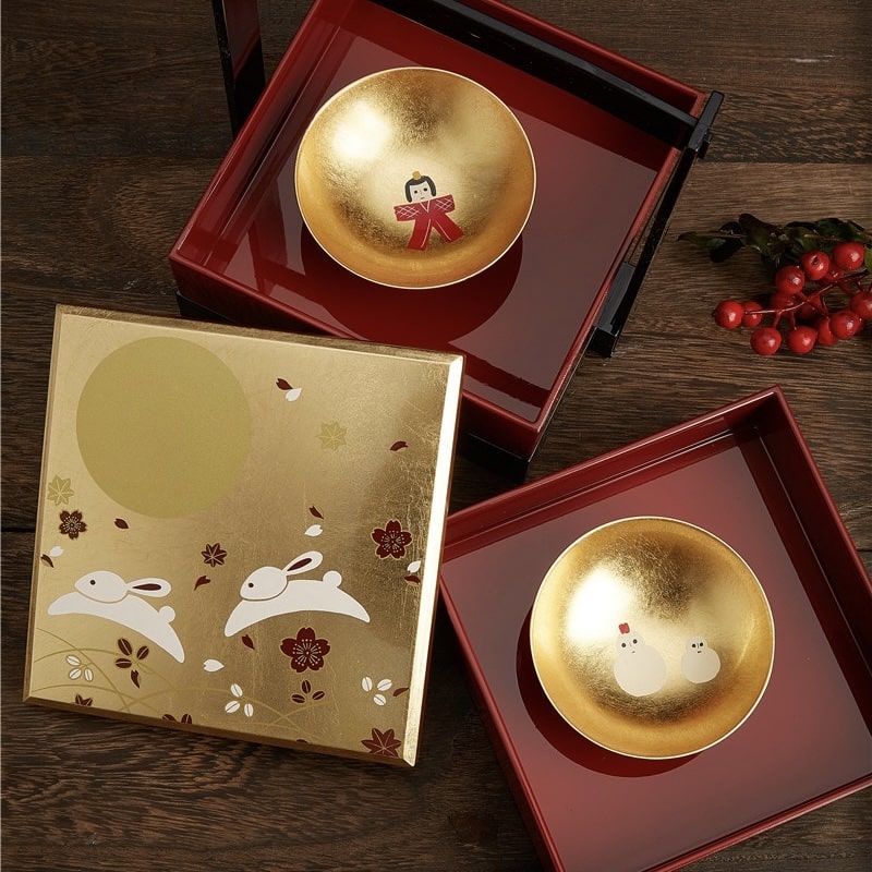 Japanese lacquerware sake cup set with gold-leaf interiors and colorful motifs.
