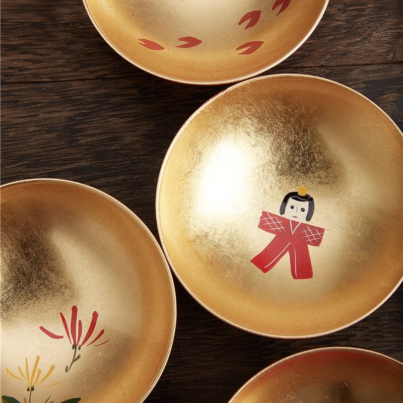 Close-up of traditional lacquer sake cups featuring seasonal icons.
