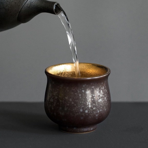 Set of four handcrafted ceramic sake cups with unique textures and earthy tones.
