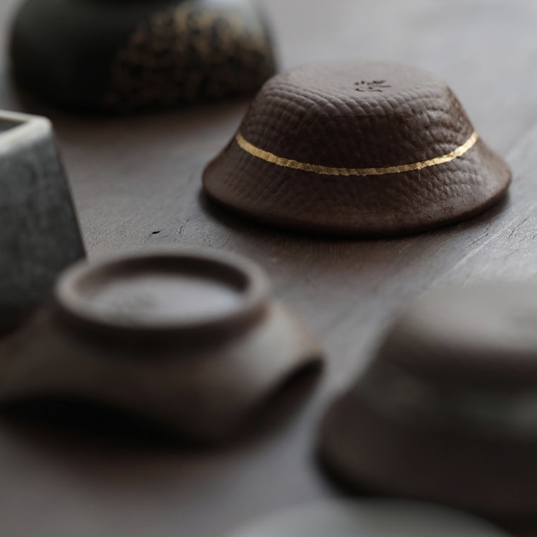 Artisan ceramic sake cups with textured finishes displayed on a neutral surface.
