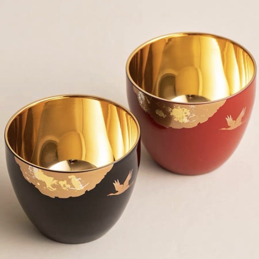 Close-up of elegant tea cups with crane motifs and radiant gold interiors.
