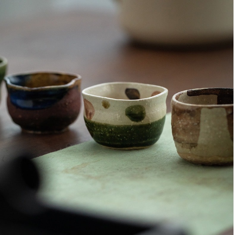 Hand-glazed ceramic tea cups in green, blue, and brown shades.
