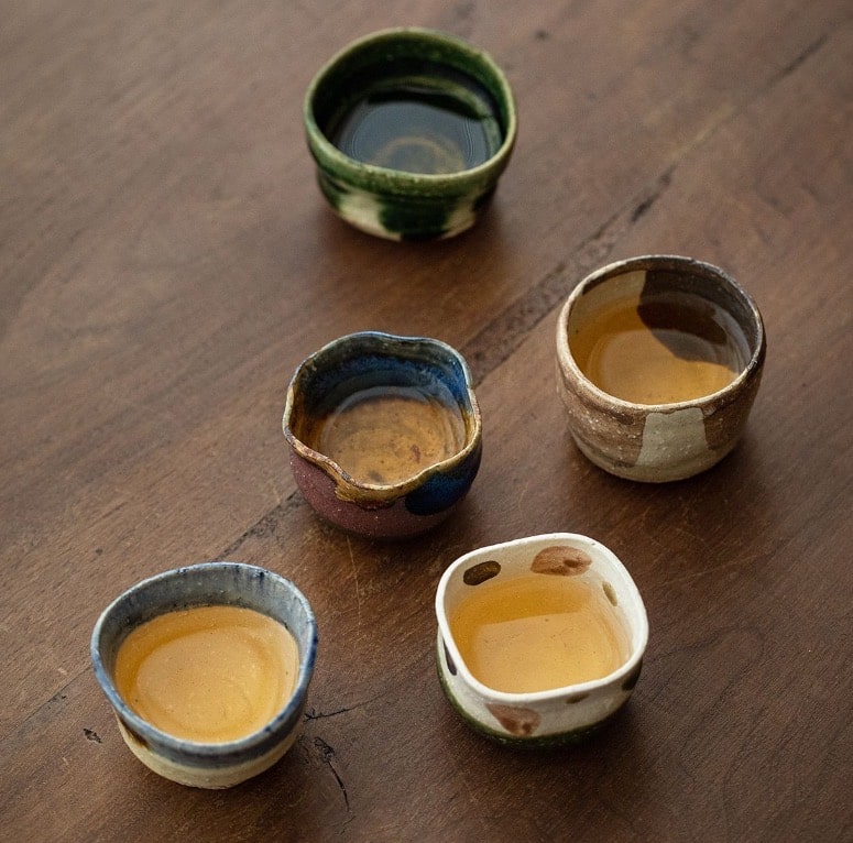 Hand-glazed ceramic tea cups in green, blue, and brown shades.
