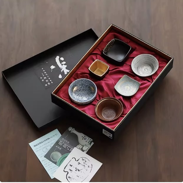 Ceramic sake set with six artisan-crafted cups in a black gift box.
