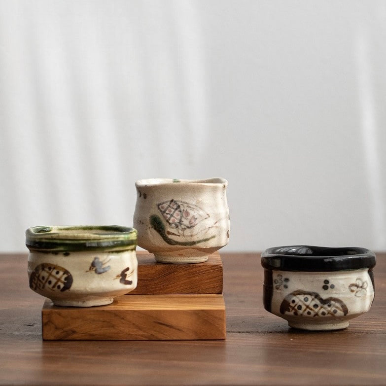 Handcrafted Japanese teacups with traditional patterns on a wooden shelf.