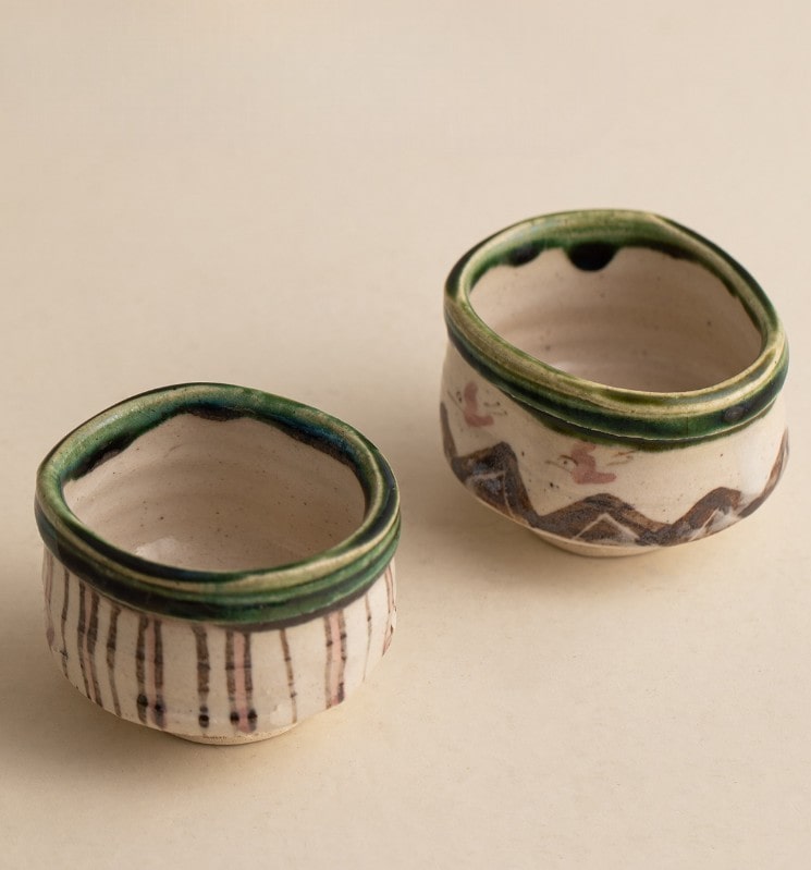 Handcrafted Japanese teacups with traditional patterns on a wooden shelf.